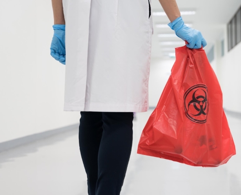 A physician walking down a hallway carrying a biohazard waste bag