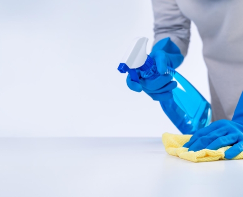 Side view of someone cleaning a surface using disinfectant spray and a cloth
